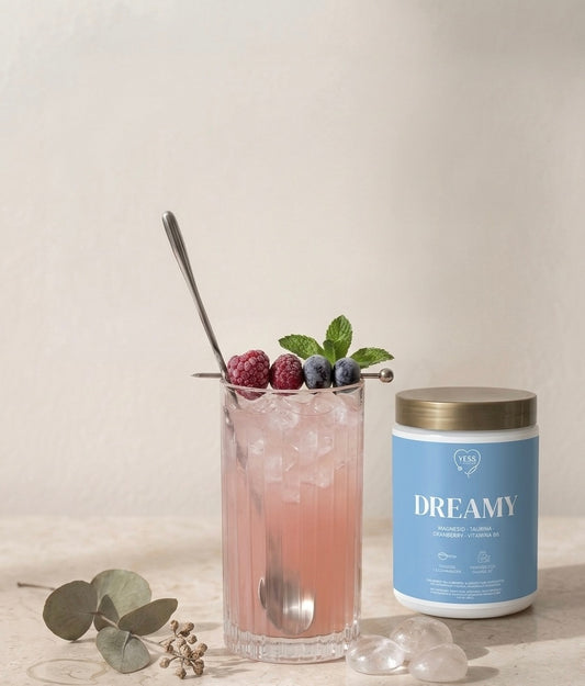 Frasco de suplemento Yess Wellness con magnesio para ayudar a dormir y lograr un sueño profundo y reparador, diluido en un vaso de agua, una bebida sabor a berries color rosa 